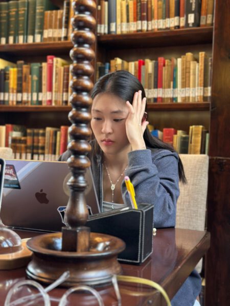 Photo of female student sitting in library doing work on a laptop.
