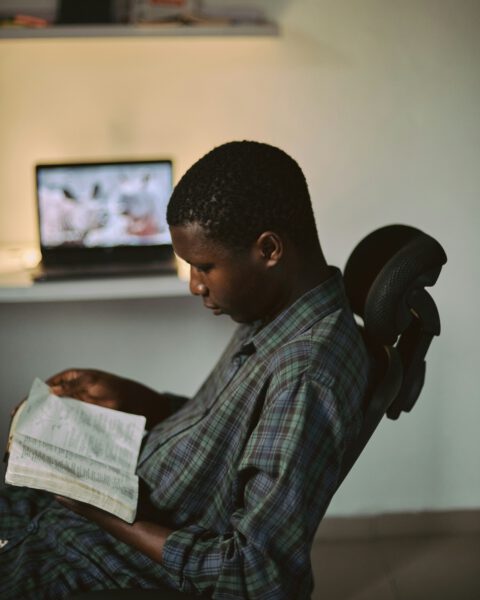 Photo of male student sitting in a desk chair with laptop in background reading the bible.