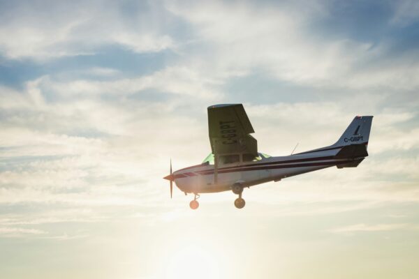 Small propeller plane flying at sunset with a bright sky and soft clouds in the background.