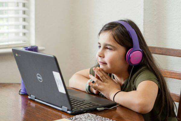 Photo of young female student with headphones on doing schoolwork on a laptop at a table.