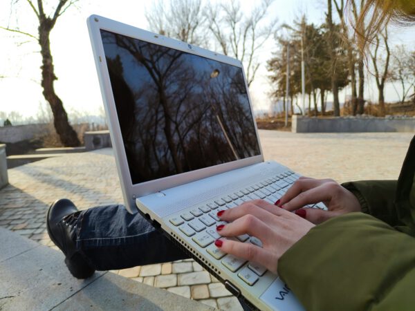 Photo of female's hands on laptop while sitting outside doing work.
