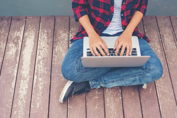 Young male hands typing laptop sitting on pier lake, relaxing working outdoor.
