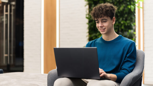A young smiling man working using a laptop while sitting in a chair in an room