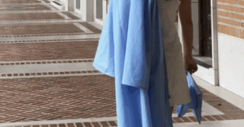 Female student standing outside holding graduation gown.